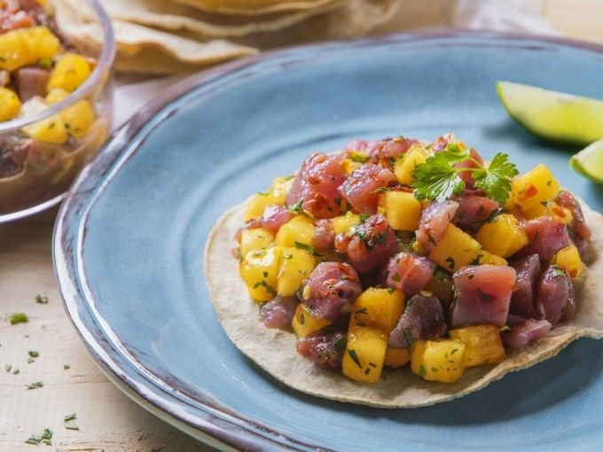 Tostada con atún fresco marinado y trozos de mango, decorada con cilantro sobre un plato azul.