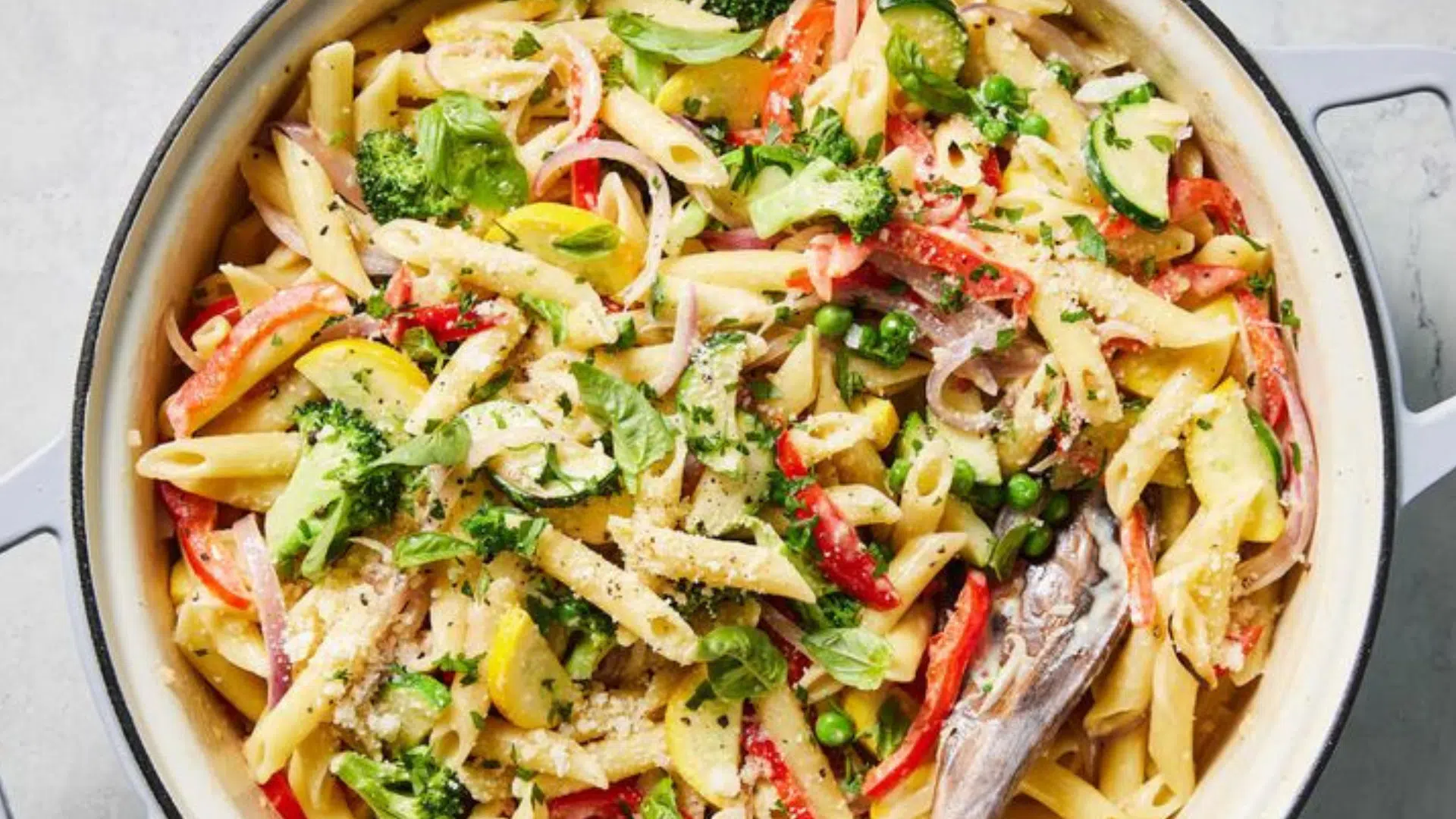 Pasta primavera con vegetales frescos como calabacitas, brócoli, pimientos y arvejas, en una cacerola.
