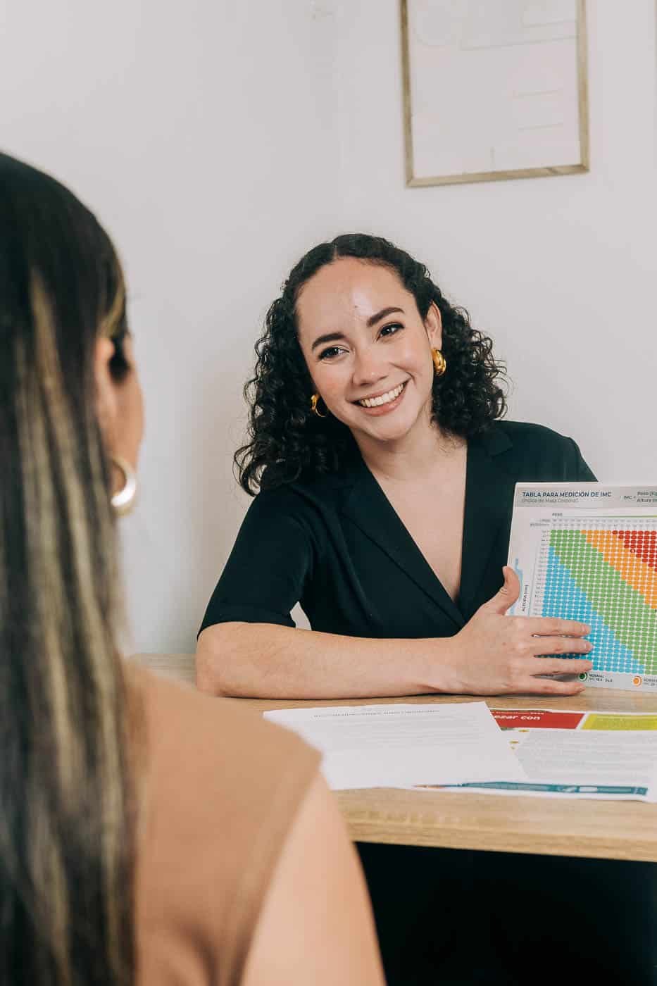 Nutricionista en consulta explicando una tabla de medición de IMC a una paciente.
