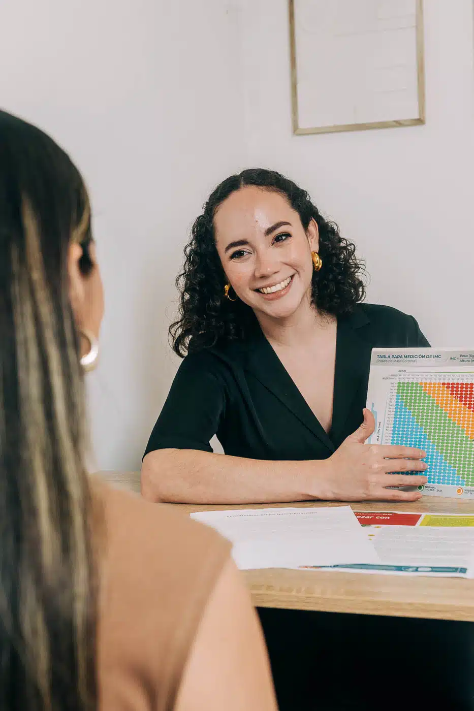 Nutricionista en consulta explicando una tabla de medición de IMC a una paciente.