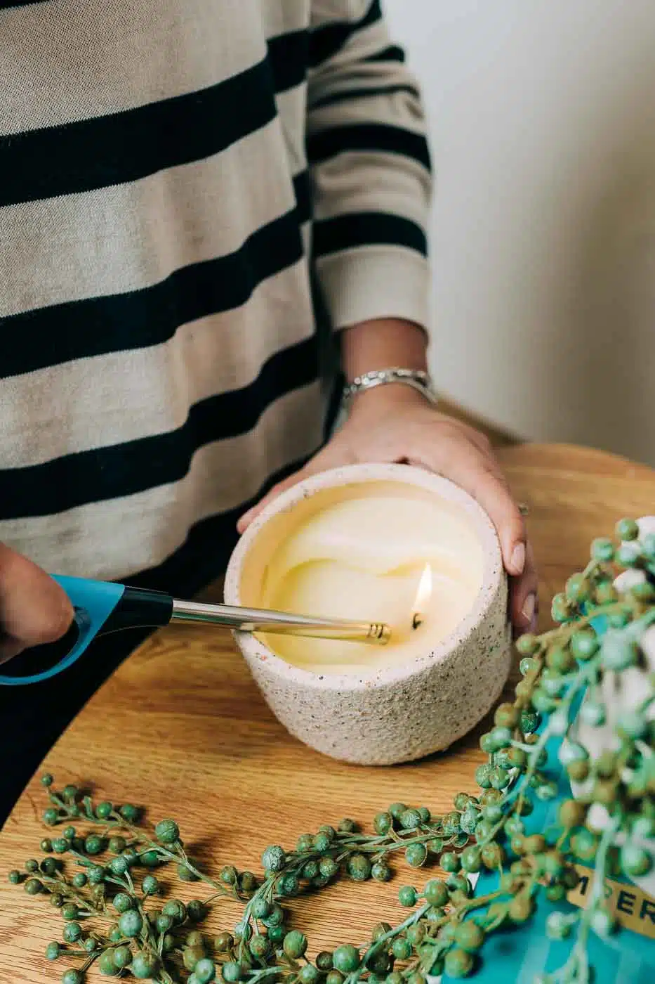 Encendido de una vela aromática sobre una mesa decorada con ramas verdes.