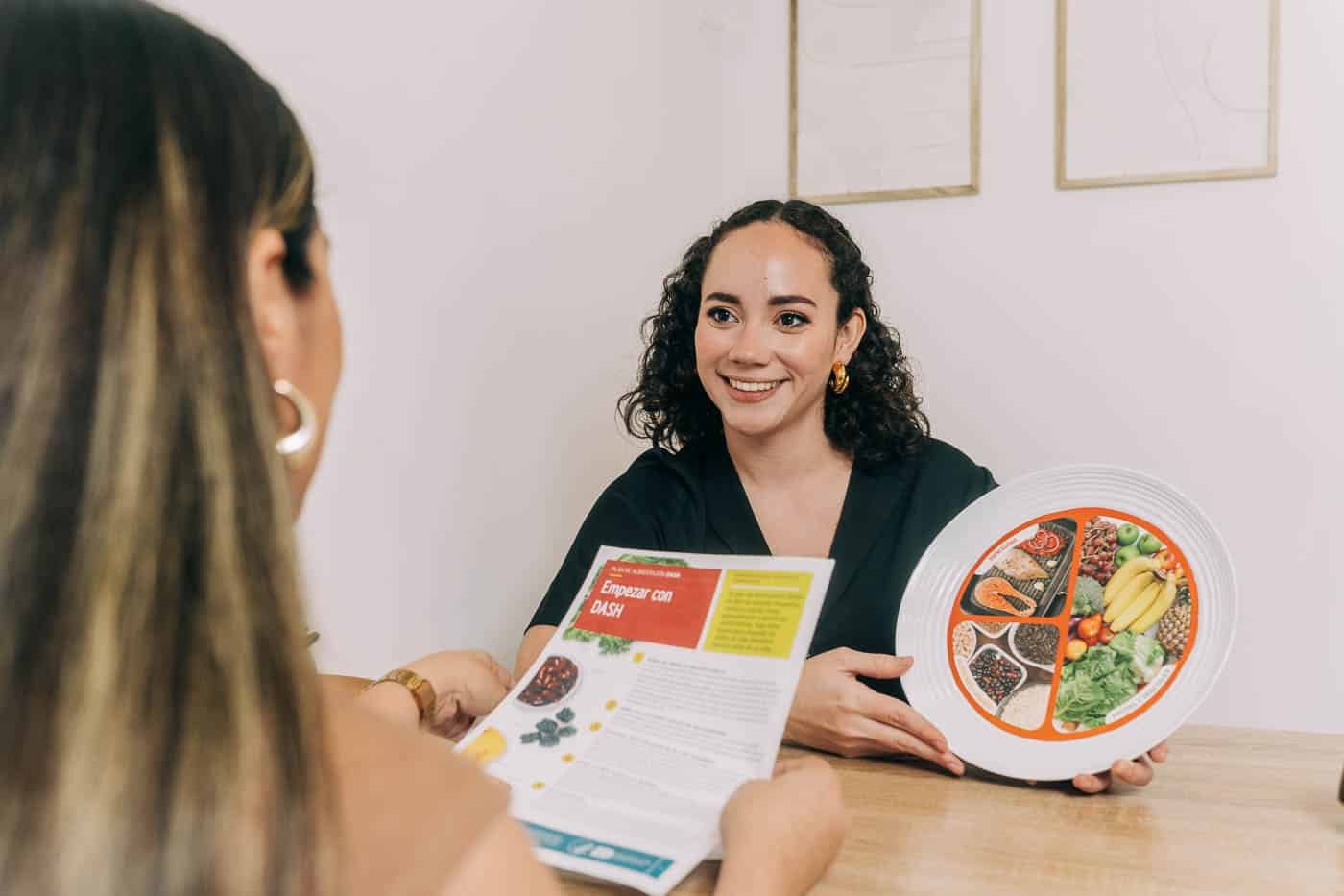Nutricionista en El Salvador explicando una dieta saludable con un plato balanceado y un folleto informativo.