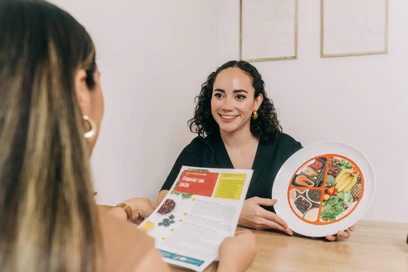 Nutricionista en El Salvador explicando una dieta saludable con un plato balanceado y un folleto informativo.