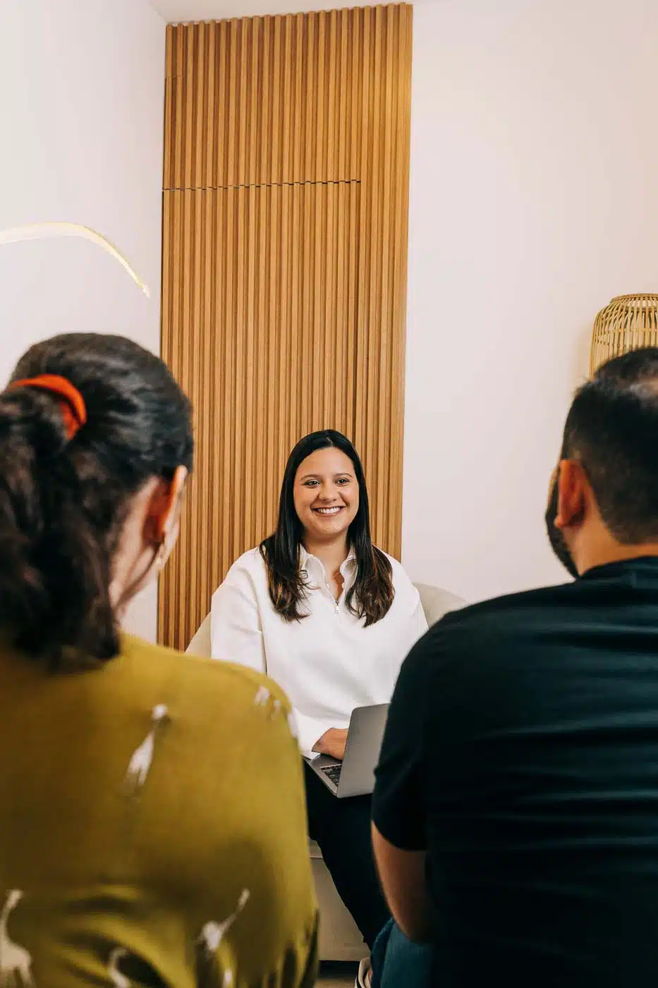 Terapia de pareja en sesión con la psicóloga Rebeca Martínez en El Salvador. Rebeca sonríe mientras conversa con una pareja sentada frente a ella en un ambiente cálido y profesional.
