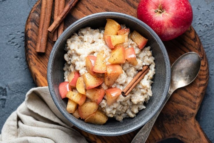 Tazón de avena con trozos de manzana caramelizada y canela en rama sobre una tabla de madera.