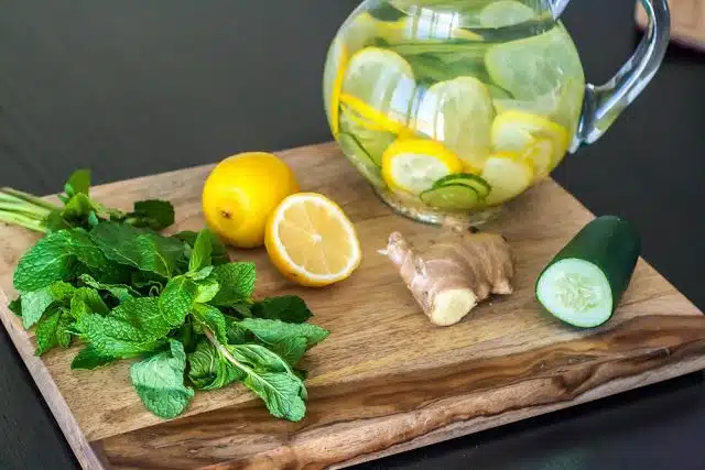 Limonada con pepino, jengibre, menta y limón en una tabla de madera junto a una jarra con agua infusionada.