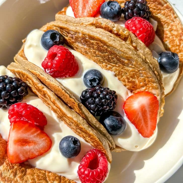 Tacos de pancakes rellenos con yogurt griego y decorados con fresas, frambuesas, moras y arándanos.